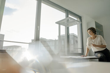 Businesswoman working in office, sitting on desk - KNSF04479