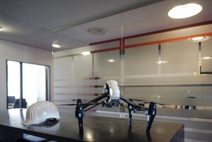 Schutzhelm und Drohne auf dem Schreibtisch im Büro eines Ingenieurs - KNSF04485