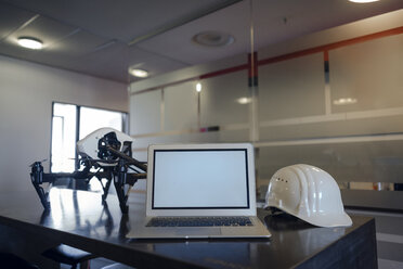 Laptop zwischen Schutzhelm und Drohne auf dem Schreibtisch im Büro eines Ingenieurs - KNSF04486