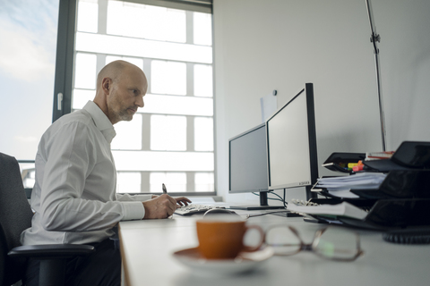 Geschäftsmann arbeitet an seinem Computer und macht sich Notizen, lizenzfreies Stockfoto