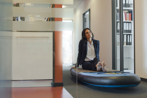 Geschäftsfrau, die auf einem Paddelbrett sitzt und im Büro träumt - KNSF04494