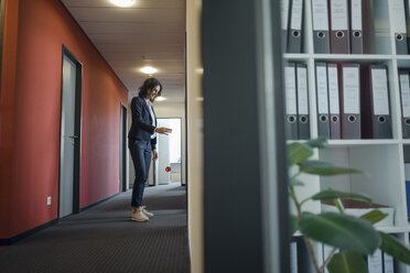 Reife Geschäftsfrau steht im Bürokorridor und spielt mit einem Jojo - KNSF04502