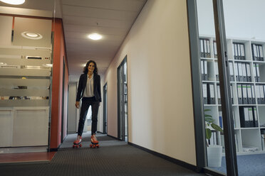 Mature businesswoman rollerskating in office corridor - KNSF04508