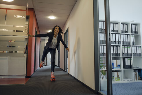 Reife Geschäftsfrau beim Rollschuhlaufen im Bürokorridor - KNSF04509