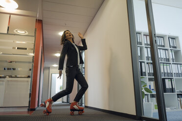 Mature businesswoman rollerskating in office corridor - KNSF04510