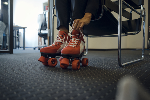 Reife Geschäftsfrau sitzt im Büro und zieht Rollschuhe an, lizenzfreies Stockfoto