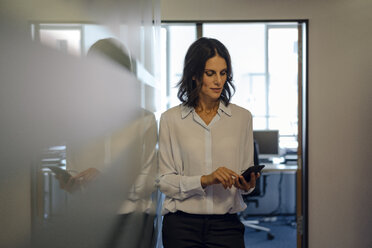 Businesswoman in office reading messages on her smartphone - KNSF04512