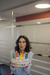 Businesswoman holding birthday cake, blowing out candles - KNSF04521