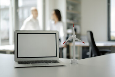 Laptop and model of wind wheel on shelf in office, with two people talking in background - KNSF04524