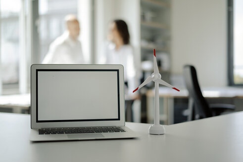 Laptop und Modell eines Windrades auf einem Regal in einem Büro, mit zwei Personen, die sich im Hintergrund unterhalten - KNSF04524
