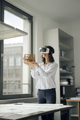 Frau hält Architekturmodell eines Hauses und benutzt eine VR-Brille - KNSF04526