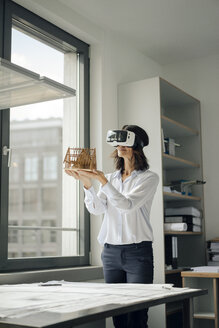 Frau hält Architekturmodell eines Hauses und benutzt eine VR-Brille - KNSF04526