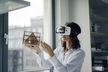 Woman holding architectural model of house, using VR glasses - KNSF04527