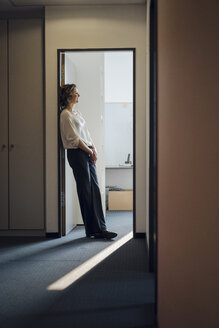 Geschäftsfrau lehnt entspannt im Türrahmen ihres Büros - KNSF04536