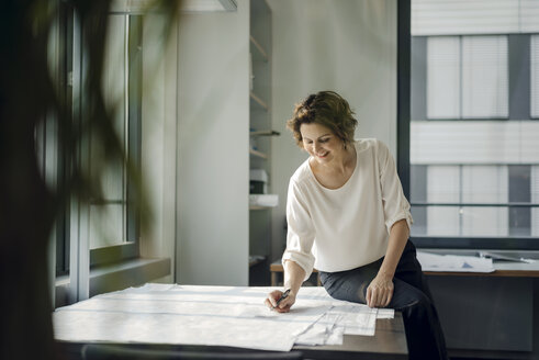 Businesswoman sitting in office, working on blueprints - KNSF04538