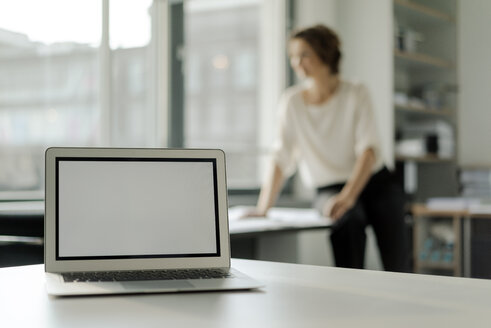 Laptop auf einem Regal, Geschäftsfrau arbeitet im Hintergrund - KNSF04544