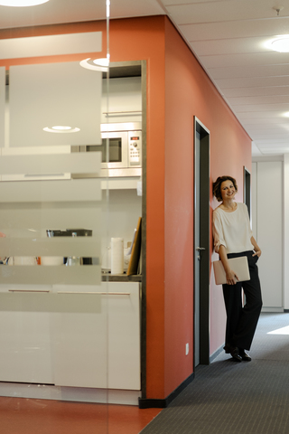 Lachende Geschäftsfrau im Bürokorridor, Laptop in der Hand, lizenzfreies Stockfoto