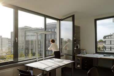 Businesswoman standing in office, looking out of window - KNSF04548