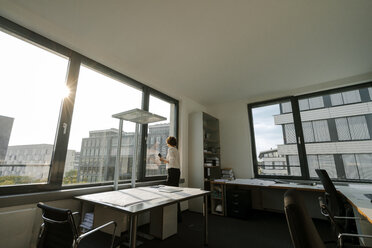 Businesswoman standing in office, looking out of window - KNSF04549