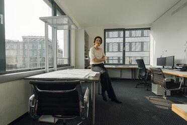 Successful businesswoman sitting on desk in her office - KNSF04554