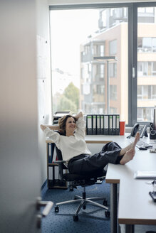 Geschäftsfrau entspannt im Büro mit Füßen auf dem Schreibtisch - KNSF04560