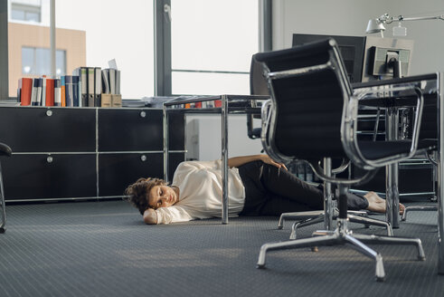 Tired businesswoman sleeping on floor under her desk - KNSF04562