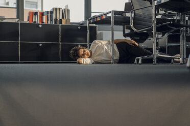 Müde Geschäftsfrau schläft auf dem Boden unter ihrem Schreibtisch - KNSF04563