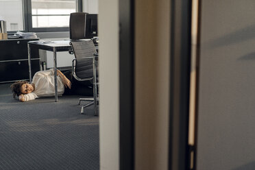 Tired businesswoman sleeping on floor under her desk - KNSF04564