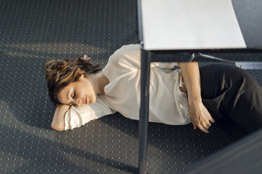 Müde Geschäftsfrau schläft auf dem Boden unter ihrem Schreibtisch - KNSF04565
