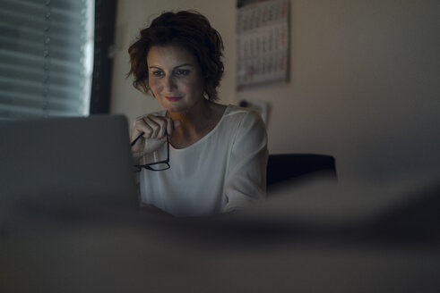 Geschäftsfrau macht Überstunden, benutzt einen Laptop, hält eine Brille - KNSF04572