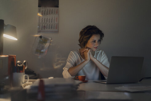Businesswoman working overtime, using laptop - KNSF04573