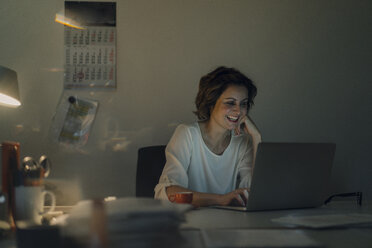 Businesswoman working overtime, using laptop - KNSF04574