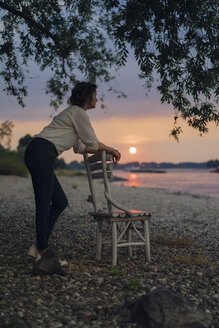 Frau lehnt auf einem Stuhl am Fluss und beobachtet den Sonnenuntergang - KNSF04581