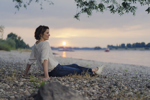 Frau sitzt am Fluss und beobachtet den Sonnenuntergang - KNSF04582