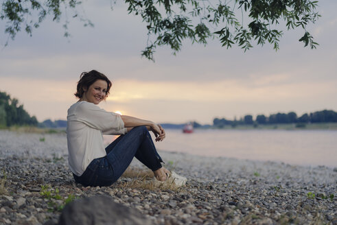 Frau sitzt am Fluss und beobachtet den Sonnenuntergang - KNSF04584