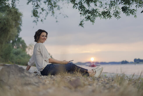 Frau sitzt am Fluss und beobachtet den Sonnenuntergang - KNSF04585