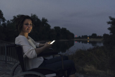 Disabled woman sitting in wheelchair, using smartphone - KNSF04595