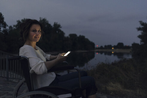 Behinderte Frau sitzt im Rollstuhl und benutzt ein Smartphone - KNSF04595