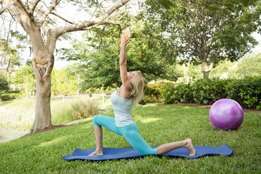 Frau macht Yoga und Pilates-Übungen auf einer Matte im Freien - AURF02212