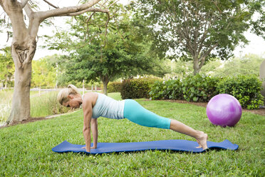 Frau macht Yoga und Pilates-Übungen auf einer Matte im Freien - AURF02213