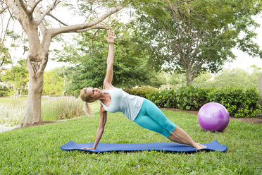 Frau macht Yoga und Pilates-Übungen auf einer Matte im Freien - AURF02215