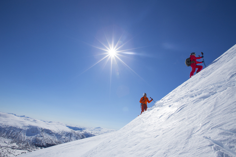 Zwei Skifahrer stehen auf einem verschneiten Berg in der Nähe des Skigebiets Myrkdalen in Fjord, Norwegen. Die Sonne scheint hell am blauen Himmel., lizenzfreies Stockfoto