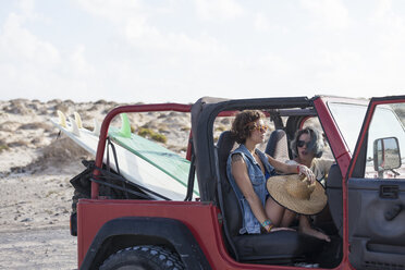 Zwei Surferinnen mit Sonnenbrille am Strand in ihrem Geländewagen, mit zwei Surfbrettern auf der Rückbank des Wagens. - AURF02254