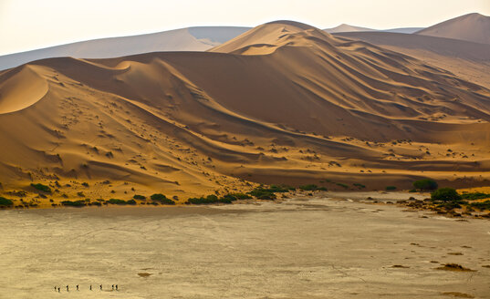 Touristen durchqueren die Salzpfanne unterhalb der roten Dünen von Sossusvlei, Namibia - AURF02260