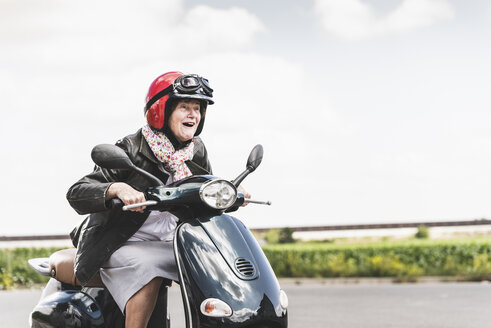 Aktive ältere Dame, die mit dem Motorroller auf der Straße fährt - UUF14930