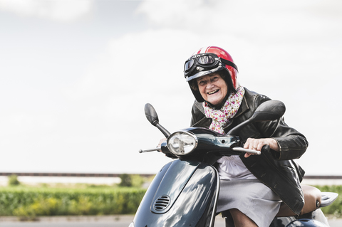 Active senior lady riding motor scooter on the road stock photo