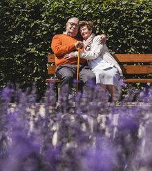 Senior couple sitting on bench in a park, with arms around - UUF14934