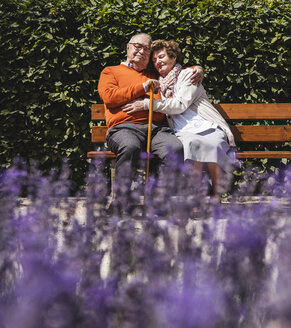 Älteres Paar auf einer Parkbank sitzend, die Arme umeinander gelegt - UUF14934