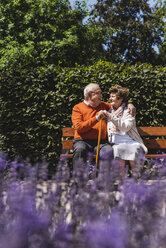 Senior couple sitting on bench in a park, falling in love - UUF14935