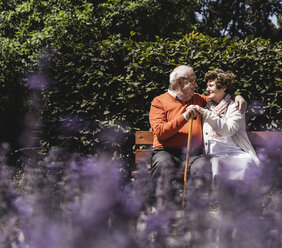 Senior couple sitting on bench in a park, falling in love - UUF14937